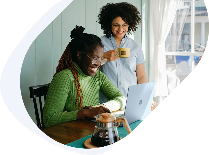 Happy woman helping her friend apply for an $800 loan with bad credit using a laptop